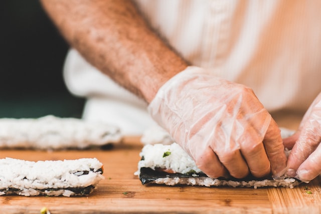 A sushi chef's hands expertly rolling a maki. 