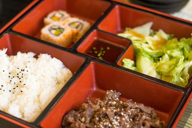 A basic bento box with rice, maki, beef slices, and lettuce.