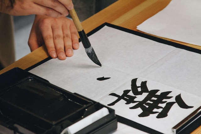 A hand holding a brush while writing characters on paper