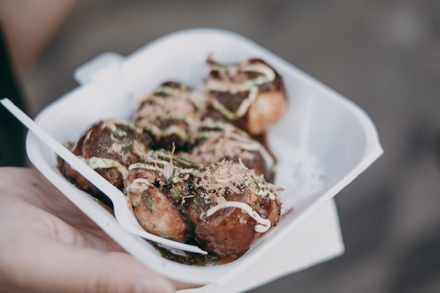 Takoyaki drizzled with mayonnaise and bonito flakes in a foam container