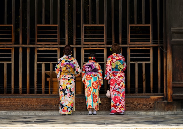 Three women wearing colorful kimonos paying their respects at a temple