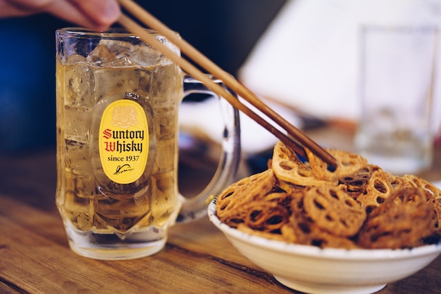 Hand picking up a lotus chip from a white ceramic bowl, a glass of ice-cold beer on the side