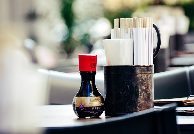 A tiny bottle of soy sauce beside  a napkin and chopstick holder on top of a table