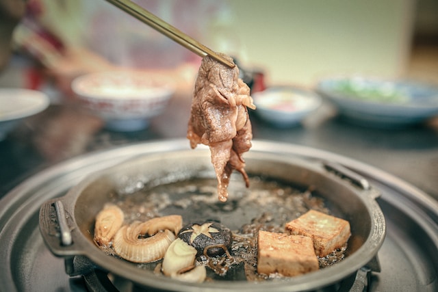 Thin sliced of meat on a chopstick over a pot of boiling broth