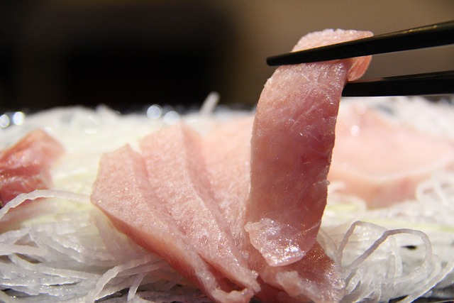 A black pair of chopsticks picking up a slice of raw tuna